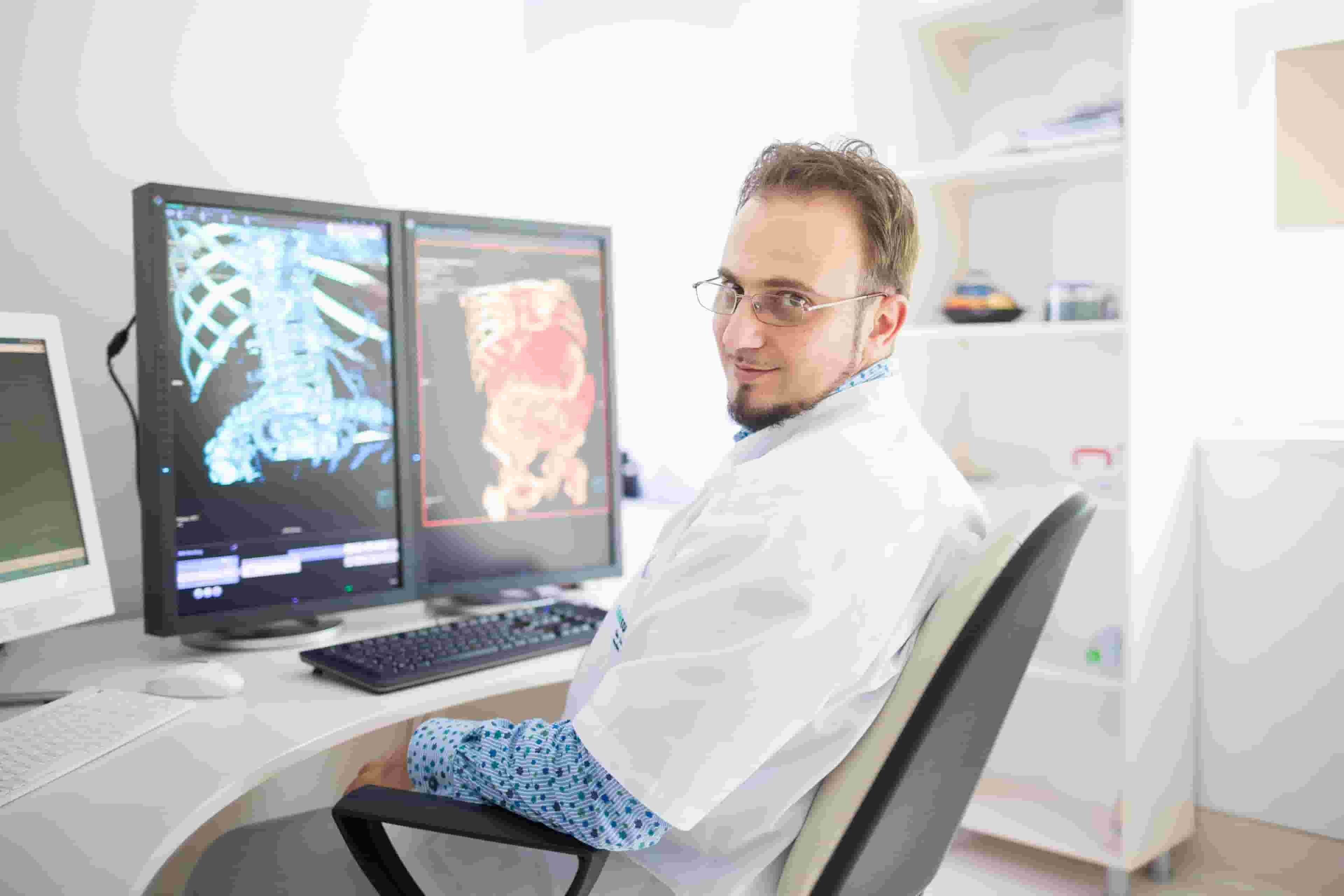 Dr. Sorin Ghiea sitting at the desk with two monitors showing medical images